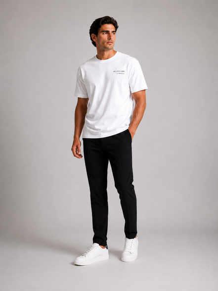 Billionaire by ORVELLA® Luxury White T-Shirt worn by a male model during a professional studio photoshoot. Premium white designer T-shirt styled with black tailored trousers and white leather sneakers, showcasing modern British luxury streetwear with a refined minimalist aesthetic.