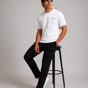 Billionaire by ORVELLA® Luxury White T-Shirt worn by a male model in a professional studio photoshoot. Premium white designer T-shirt paired with black tailored trousers and white sneakers, showcasing modern British luxury streetwear.