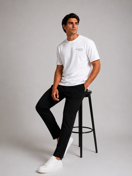 Billionaire by ORVELLA® Luxury White T-Shirt worn by a male model in a professional studio photoshoot. Premium white designer T-shirt paired with black tailored trousers and white sneakers, showcasing modern British luxury streetwear.