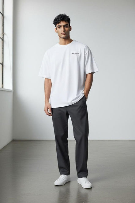 Man wearing the Billionaire by Orvella white t-shirt and dark pants standing in a minimalistic room.
