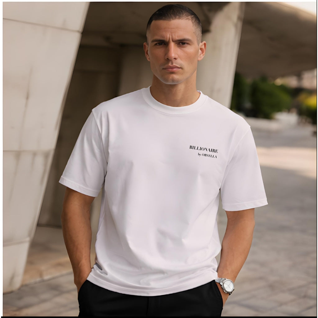 Man wearing a white t-shirt with Billionaire by Orvella brand logo, standing outdoors.