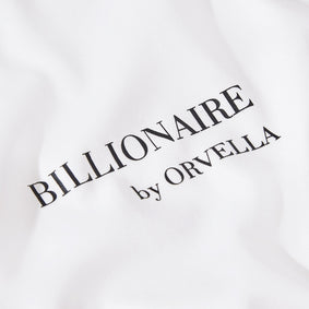 Close-up of the Billionaire by ORVELLA white luxury T-shirt chest print, showing refined black branding on smooth premium fabric.
