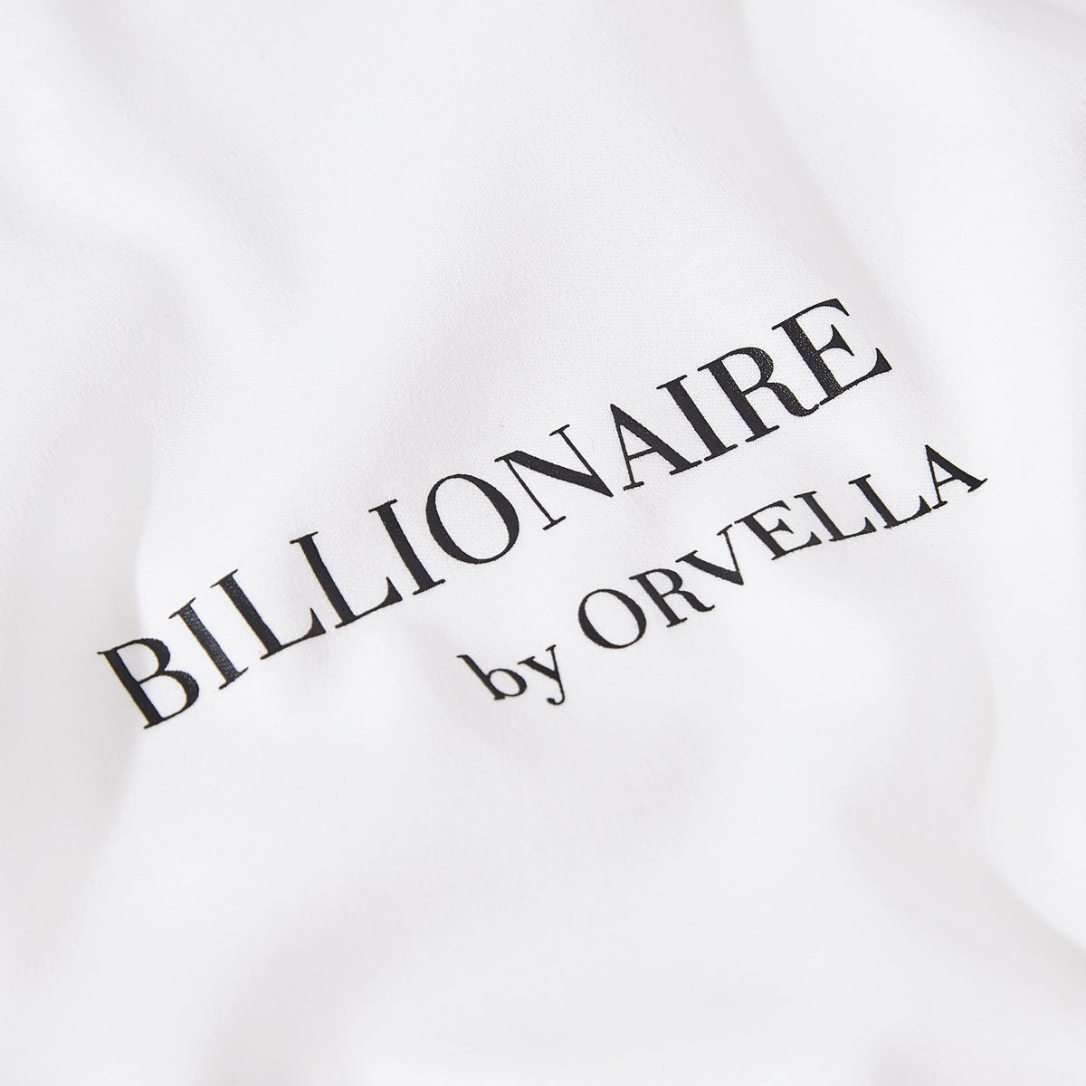 Close-up of the Billionaire by ORVELLA white luxury T-shirt chest print, showing refined black branding on smooth premium fabric.
