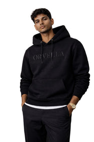 Male model wearing a black ORVELLA luxury hoodie with tonal chest branding, drawstring hood, front pouch pocket, and premium streetwear styling.