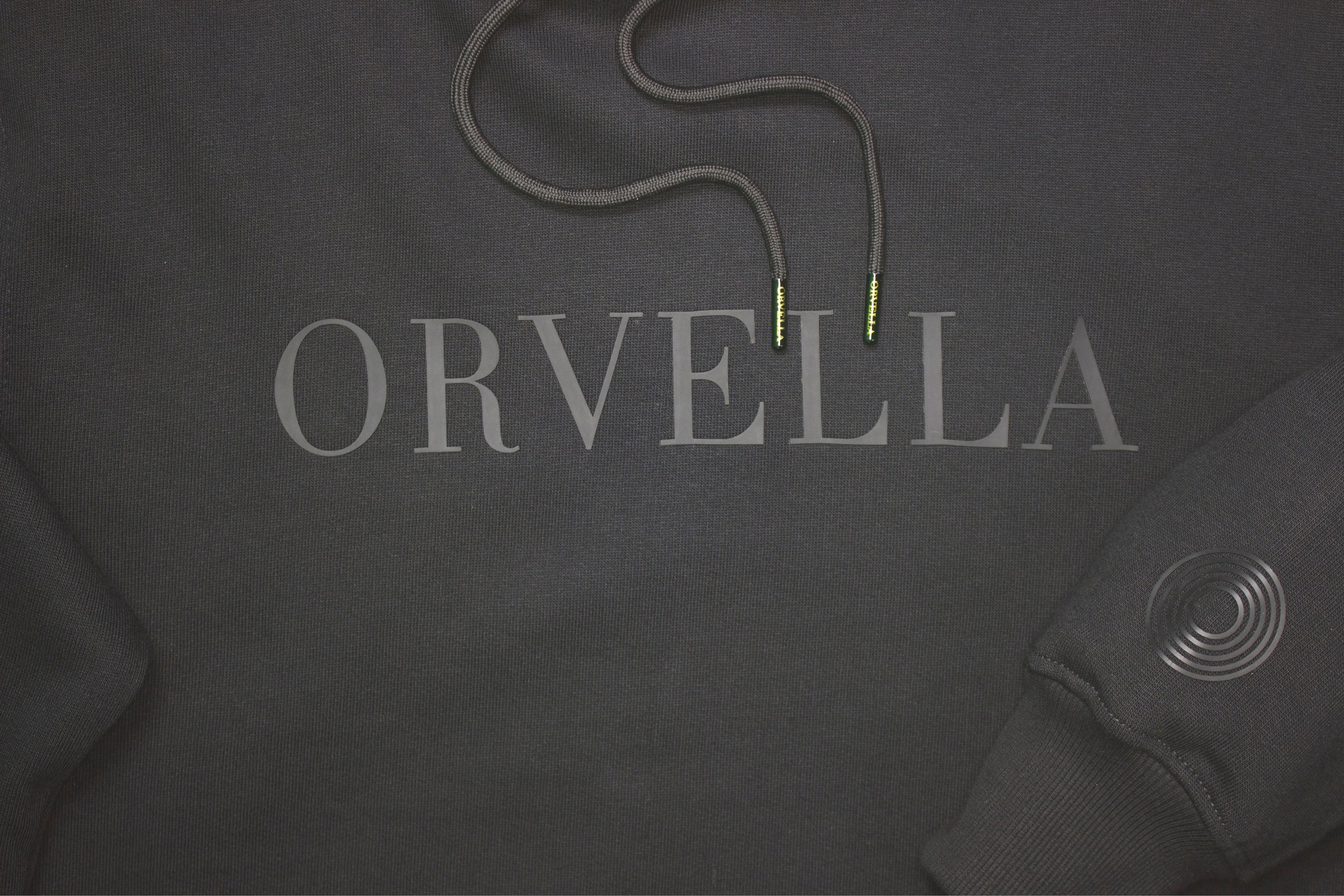 Luxury black ORVELLA hoodie close-up with tonal chest logo, branded aglets and signature sleeve emblem
