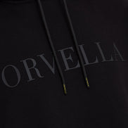Close-up of the black ORVELLA luxury hoodie showing tonal chest branding, textured fabric, drawstrings, and branded aglet details.