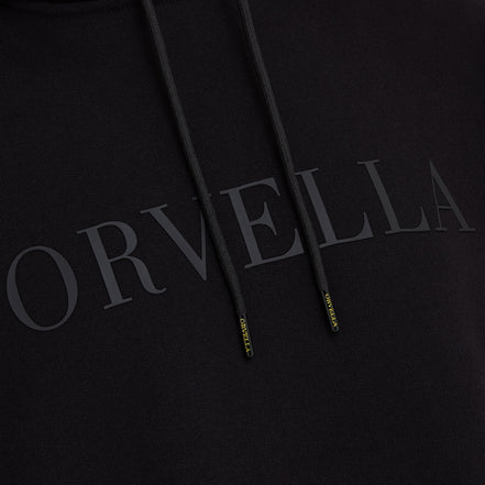 Close-up of the black ORVELLA luxury hoodie showing tonal chest branding, textured fabric, drawstrings, and branded aglet details.