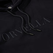 Close-up of the black ORVELLA luxury hoodie showing tonal chest branding, textured heavyweight fabric, drawstring hood, and branded aglet details.