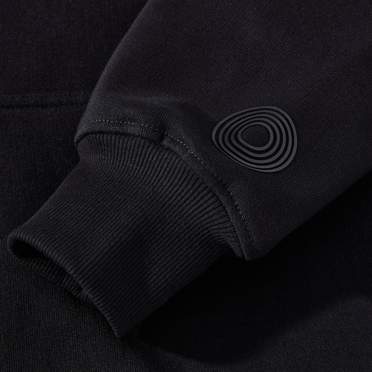 Close-up of the black ORVELLA luxury hoodie sleeve showing ribbed cuff detail, premium fabric texture, and subtle tonal signature emblem.