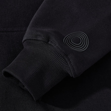Close-up of the black ORVELLA luxury hoodie sleeve showing ribbed cuff detail, premium fabric texture, and subtle tonal signature emblem.