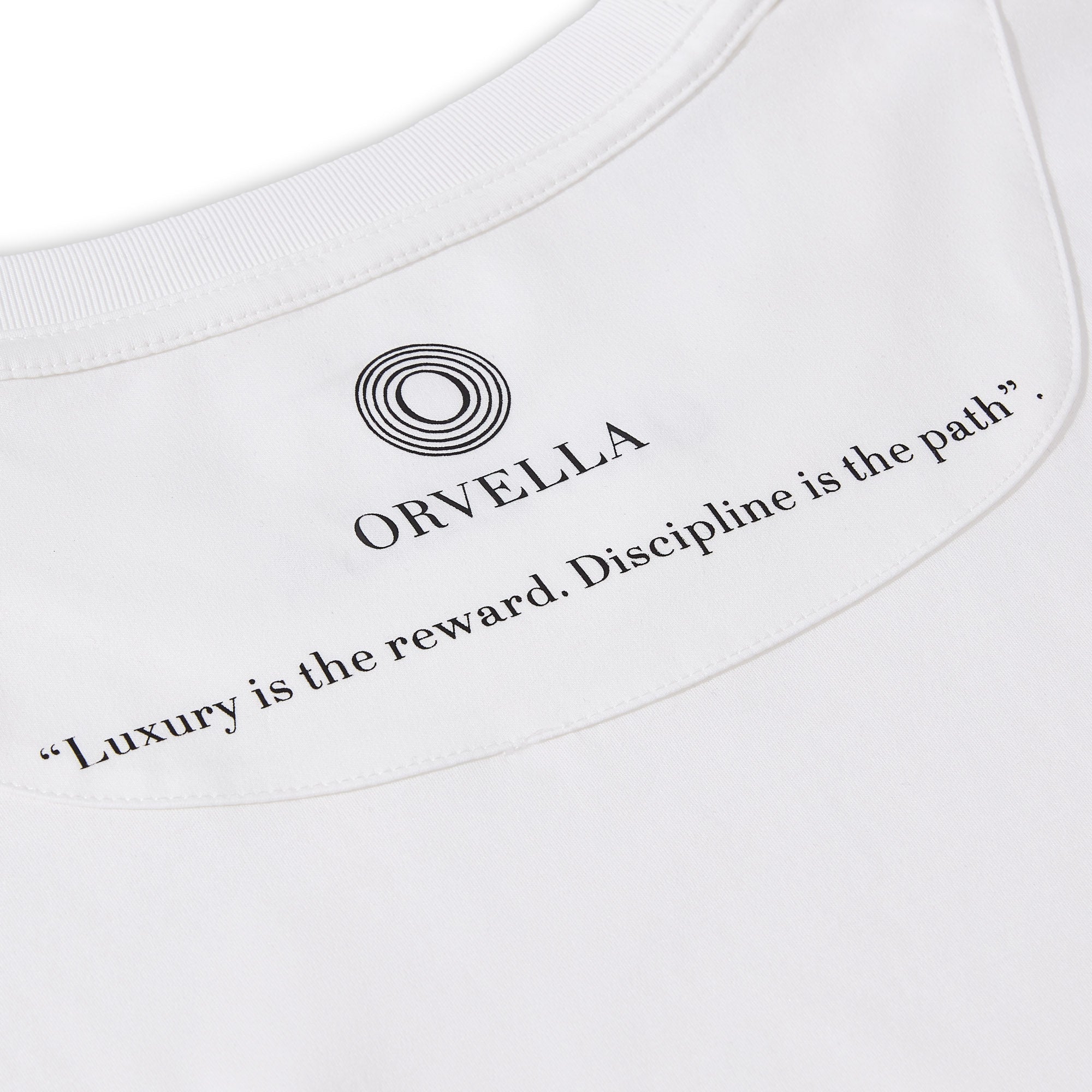 Close-up of the Billionaire by ORVELLA white luxury T-shirt inner neck print, showing the ORVELLA logo, clean collar stitching, and the quote “Luxury is the reward. Discipline is the path.”